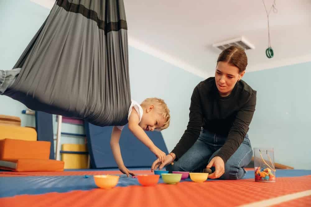 Putting the objects into bowls while hanging. Preschool child with teacher during developmental activities in a playroom.